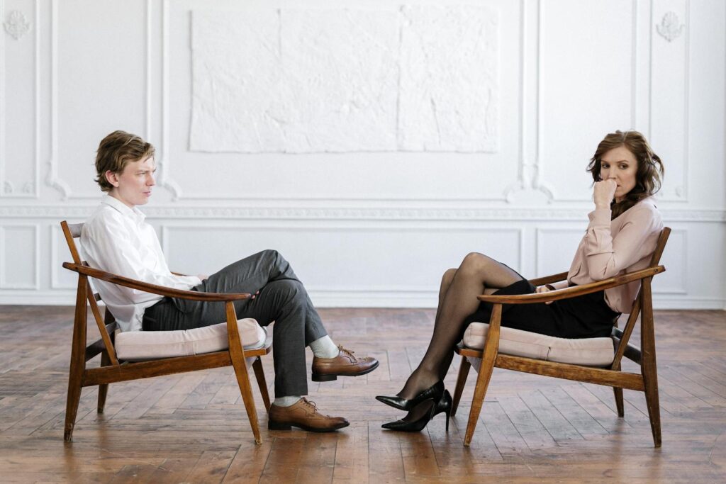 Man and woman in professional consultation setting, sitting across each other in modern office.