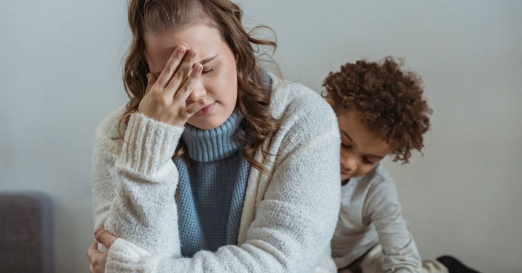 Una madre con expresión cansada cuidando a sus hijos en casa, reflejando el agotamiento emocional que puede sentir al criar.