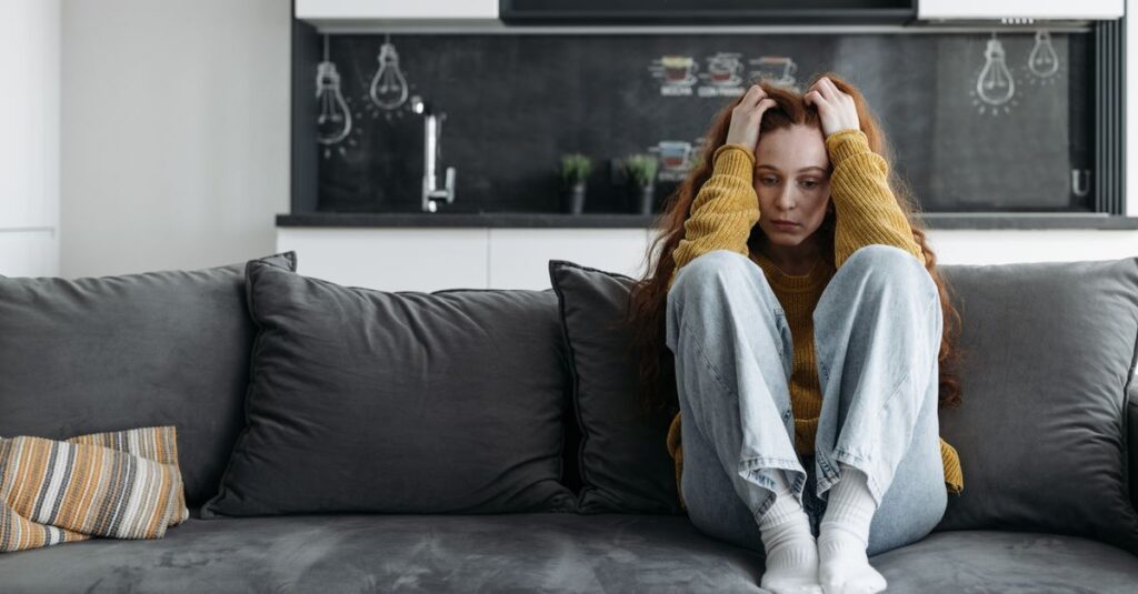 Una persona sentada en un sofá con una expresión triste, simbolizando el impacto de la tristeza en la vida diaria.